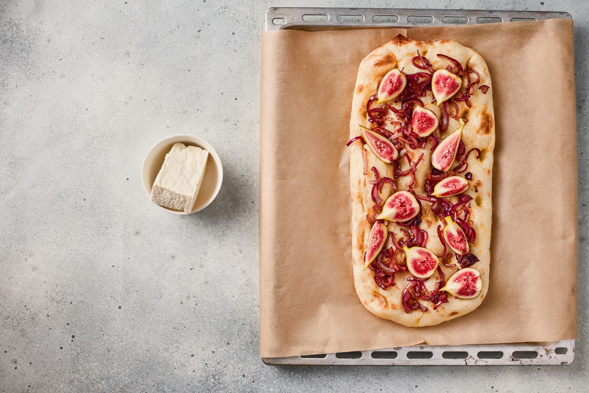 Fresh fig wedges arranged over caramelized red onions on flatbread before baking.