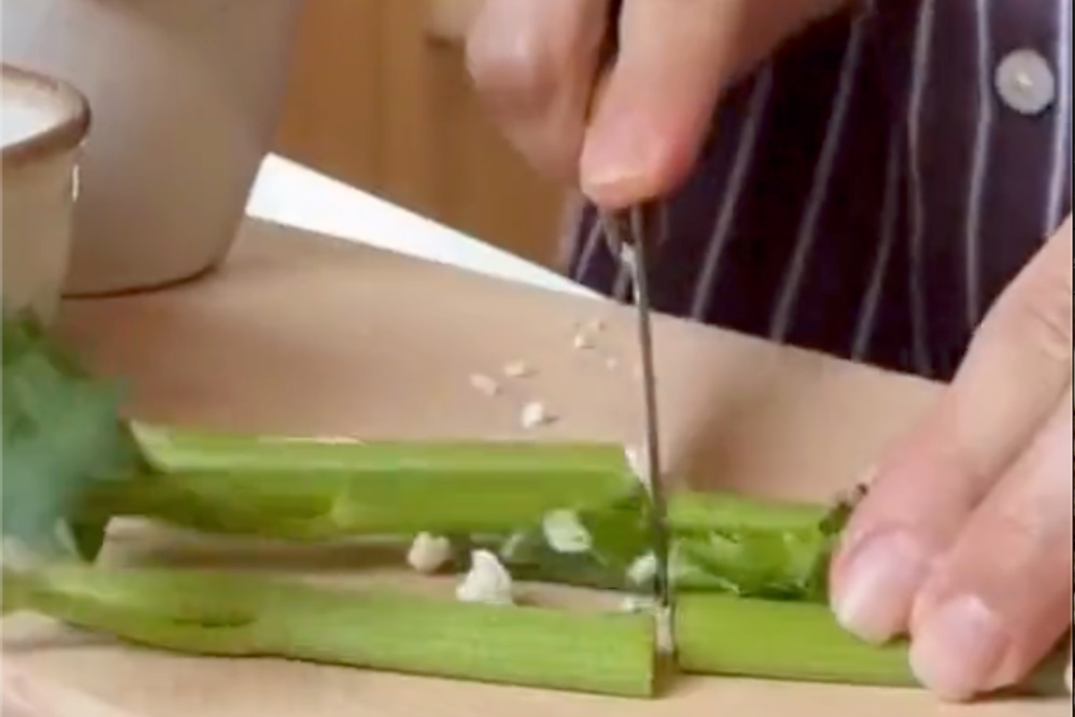 Hands chopping fresh green herbs on a cutting board while preparing ingredients for Mediterranean olive salad with creamy labneh.