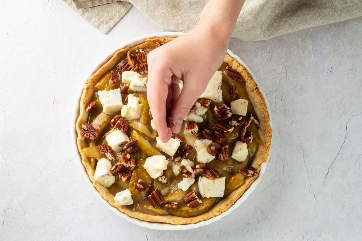 Chopped pecans being sprinkled over a pear and Gorgonzola tart before baking.
