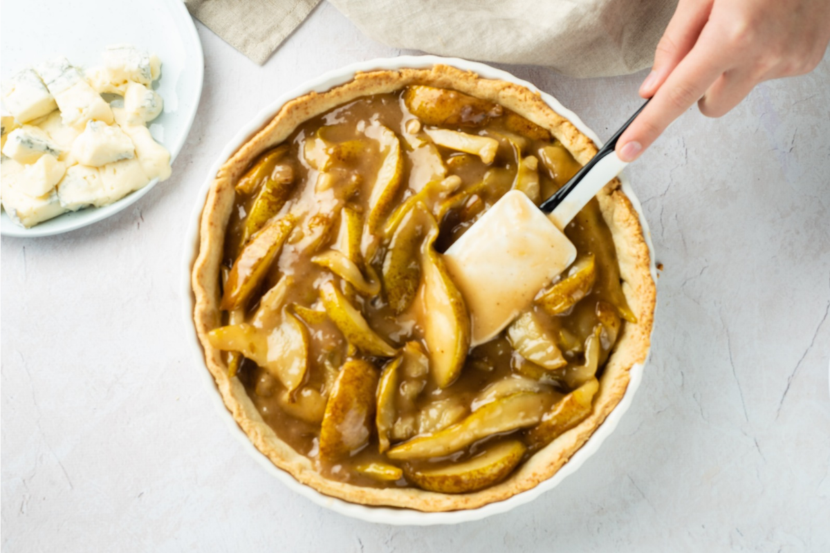 Cooked pear filling being spooned into a baked tart crust.