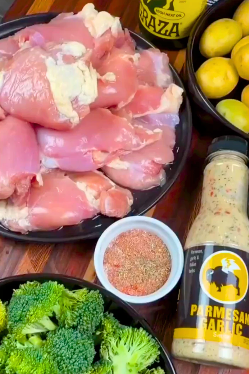 Ingredients for sheet pan garlic Parmesan chicken thighs, including raw chicken, baby potatoes, fresh broccoli, seasonings, and Parmesan Garlic sauce.