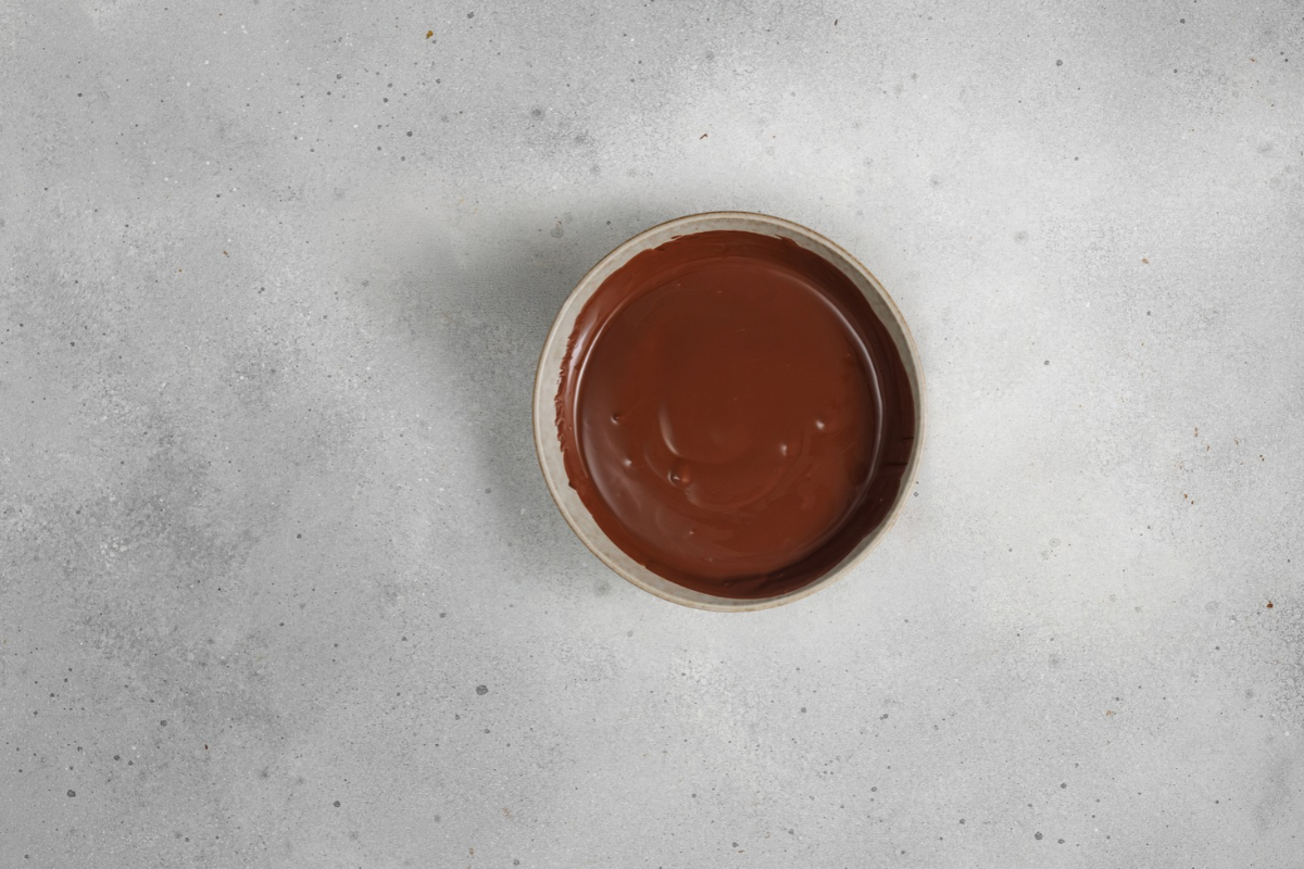 Smooth melted chocolate glaze in a ceramic bowl, ready to drizzle over homemade chocolate marble Bundt cake.

