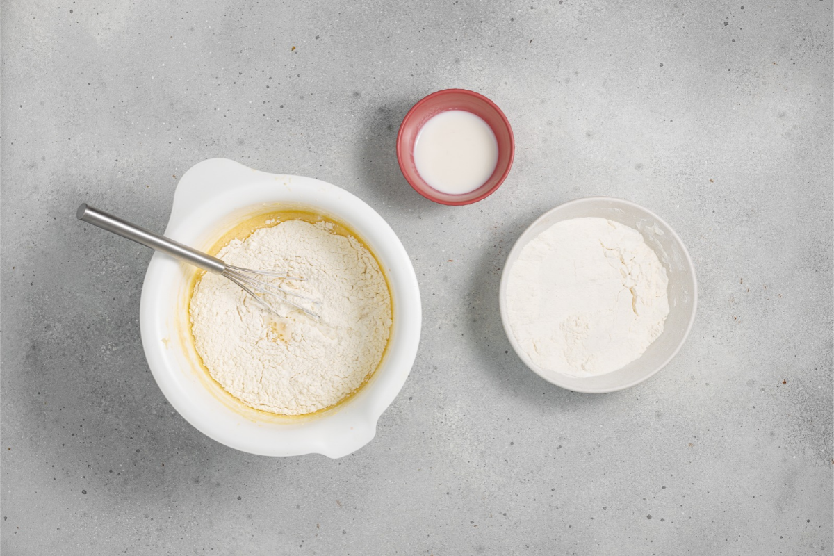 Flour being incorporated into the yellow cake batter with a whisk in a white mixing bowl
