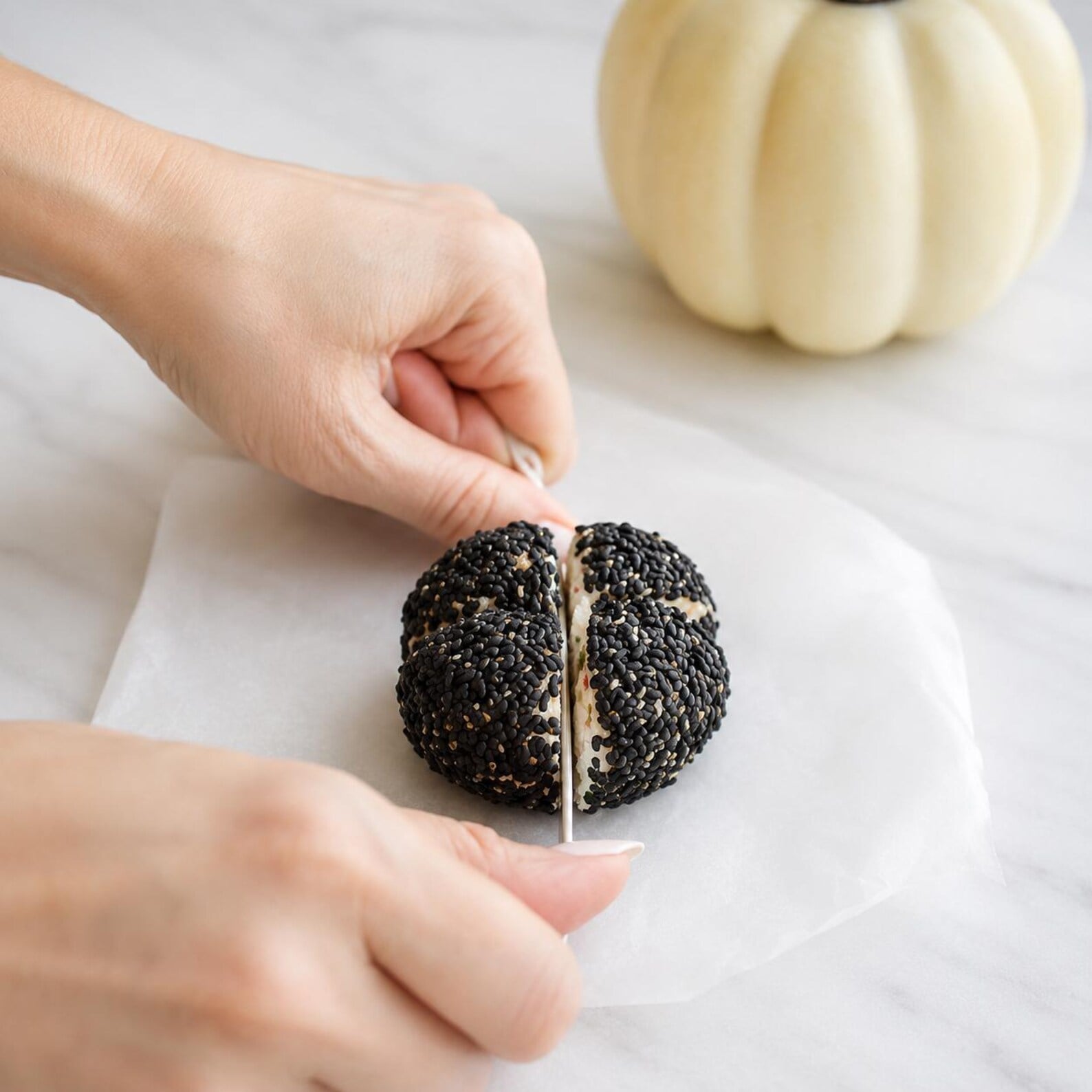 Black sesame-coated cheese ball being shaped with vertical grooves to resemble a mini pumpkin for a festive Fall, Autumn, and Thanksgiving appetizer.
